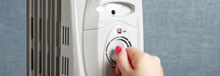 Eine Hand stellt die Temperatur an einem Ölradiator ein.